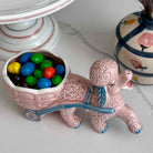 Ceramic poodle figurine with a cart full of colorful candies on a light surface.