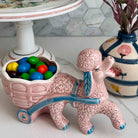Ceramic poodle with a cart full of colorful candies on a marble surface.