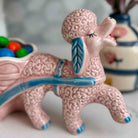 Pink ceramic poodle with a blue ribbon on a white surface