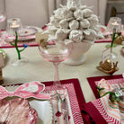 Decorative table setting with floral centerpiece, pink glassware, and patterned place mats.