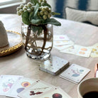 Playing cards with floral designs on a table with a vase and cup.