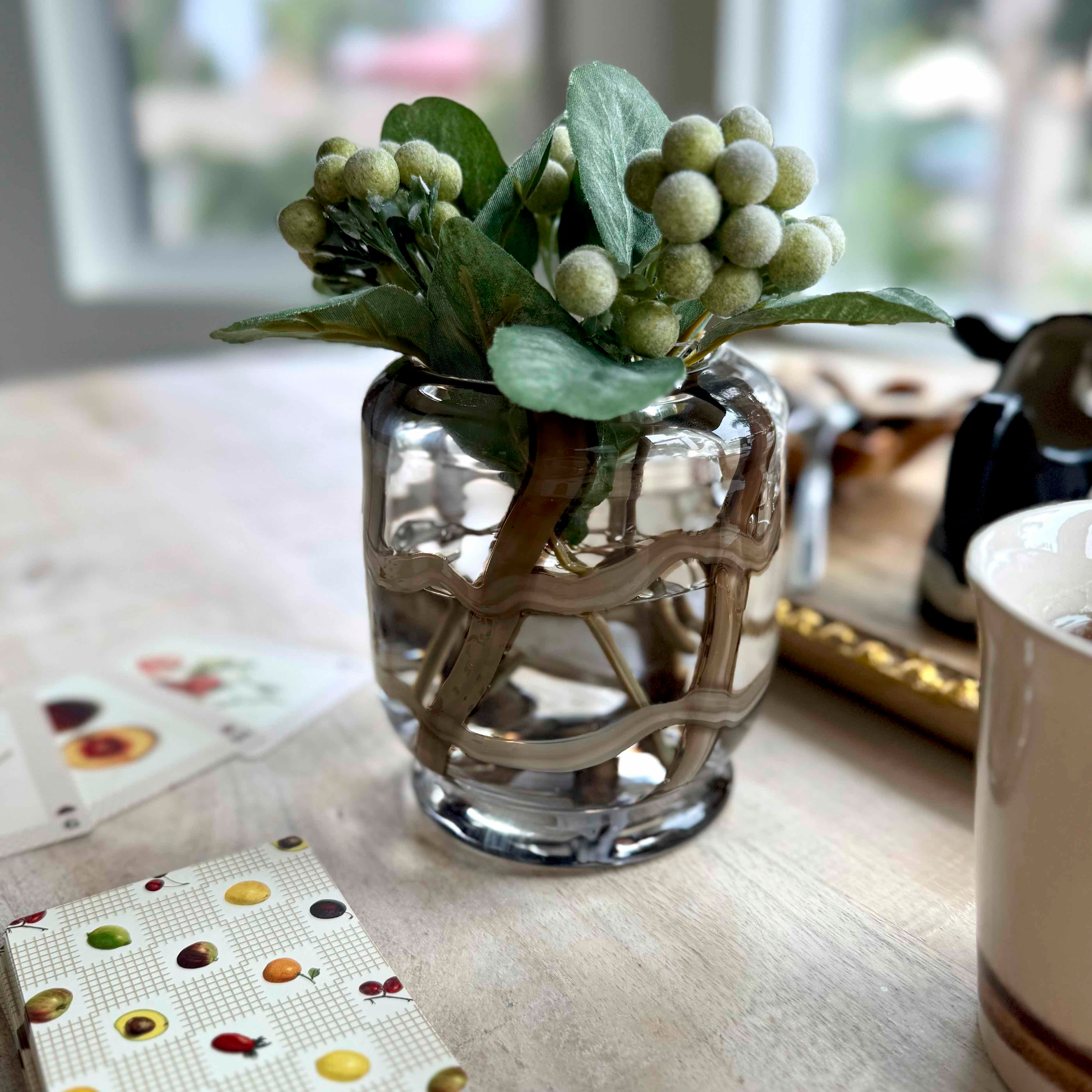 Small glass vase with decorative greenery on a table
