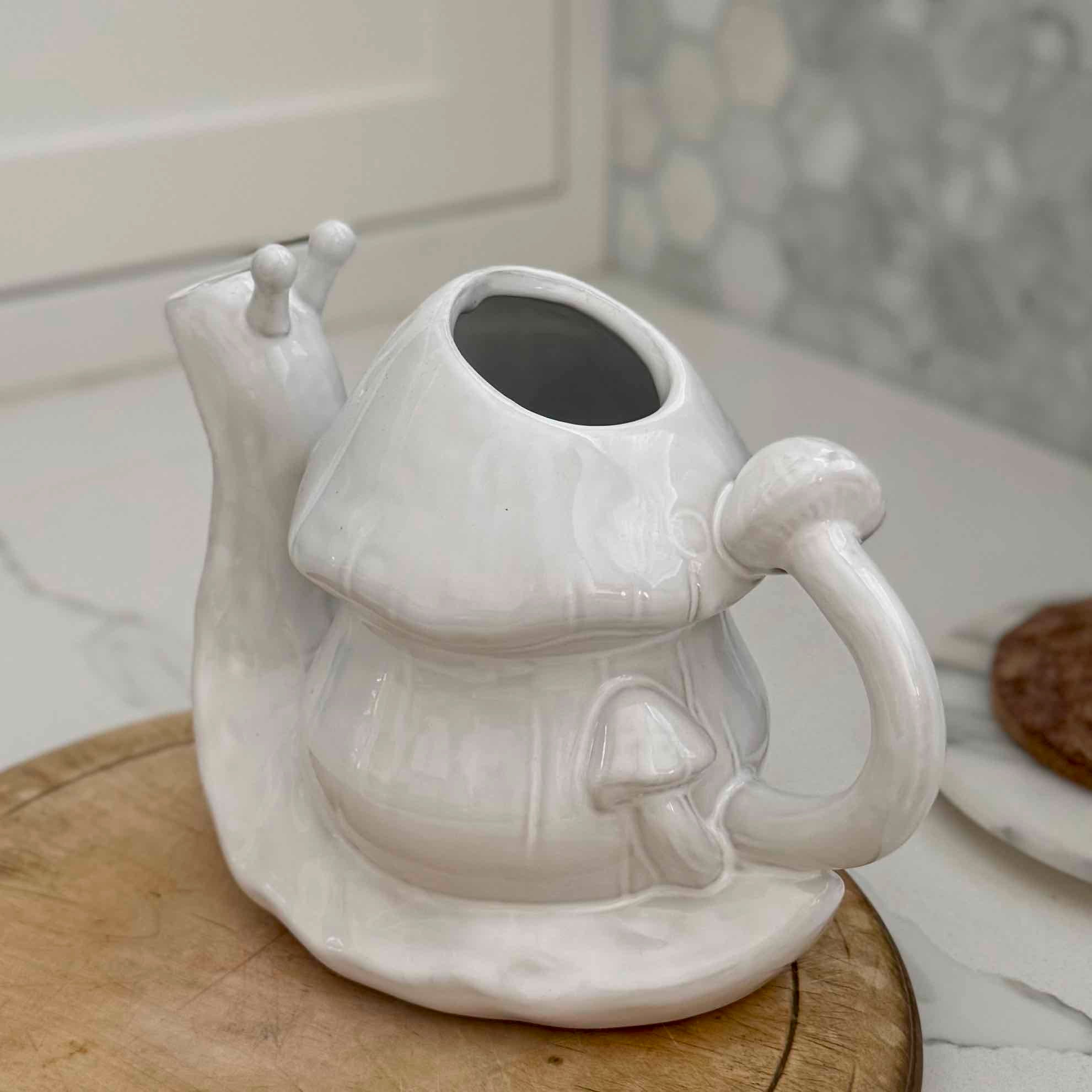 White ceramic teapot shaped like a mushroom on a wooden surface.