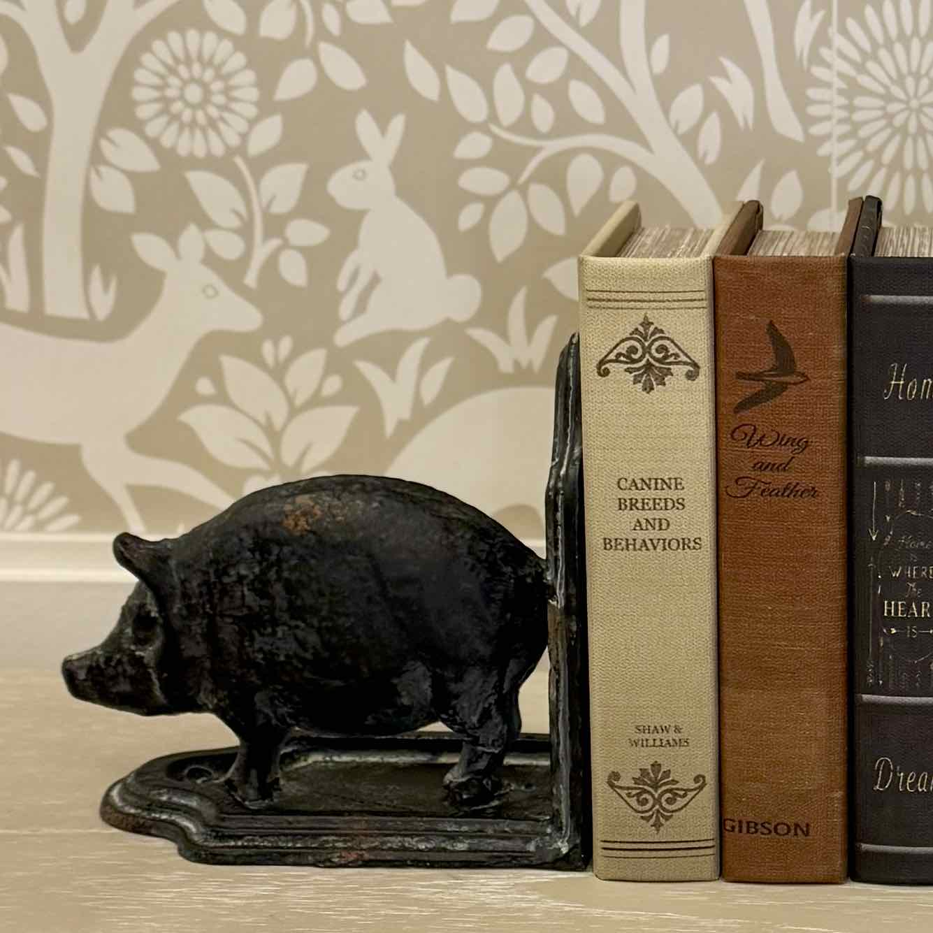 Decorative black pig bookend with books on a surface against a patterned wall.