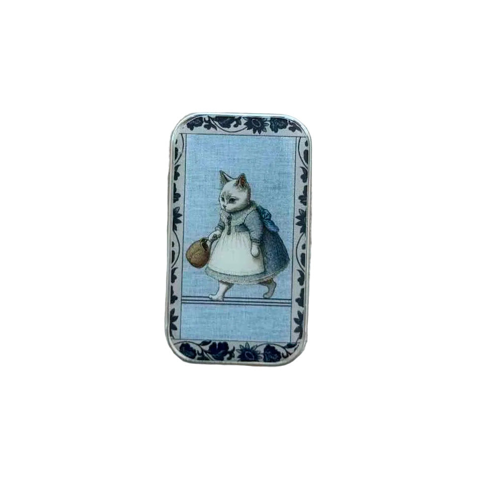 A small rectangular tin with a vintage illustration of a cat in a dress holding a basket, placed on a light wood surface.