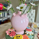 Pink vase with flowers on a table with cookies in the background