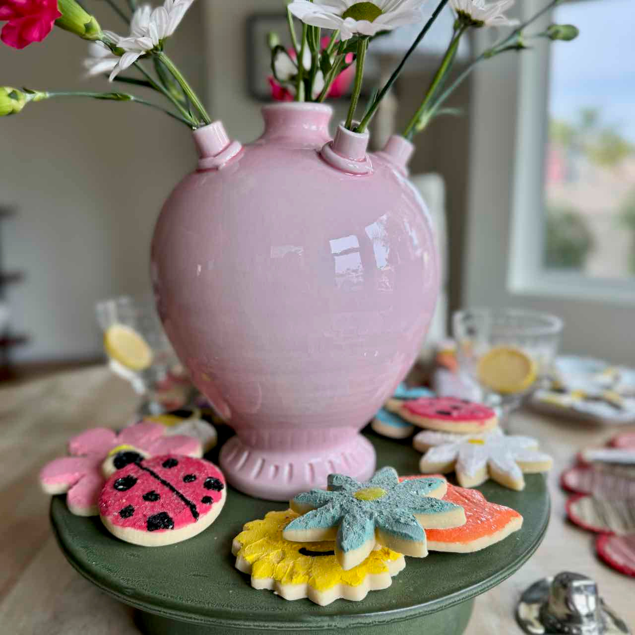 Pink vase with flowers on a green stand with decorative cookies
