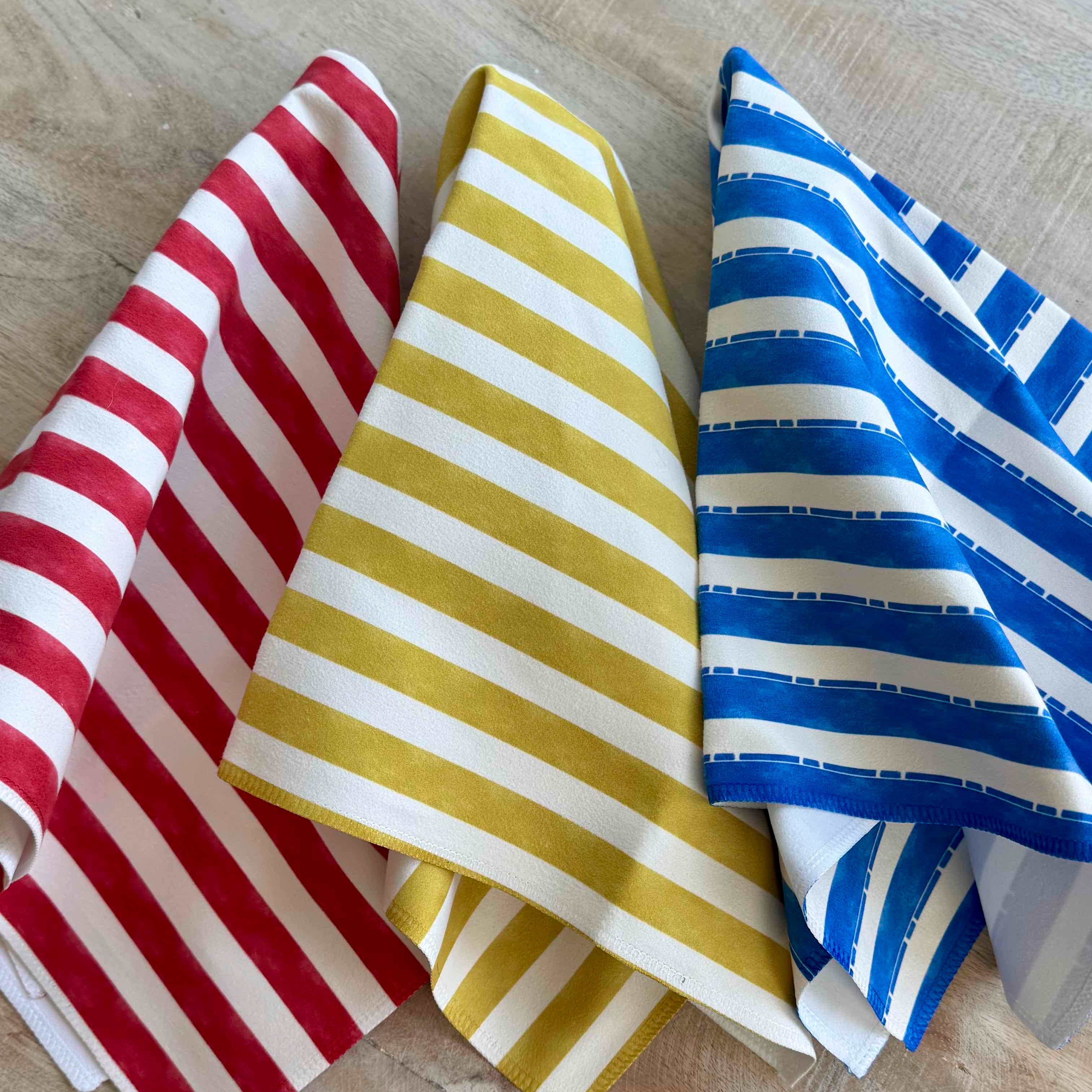 Three striped fabric samples in red, yellow, and blue on a wooden surface