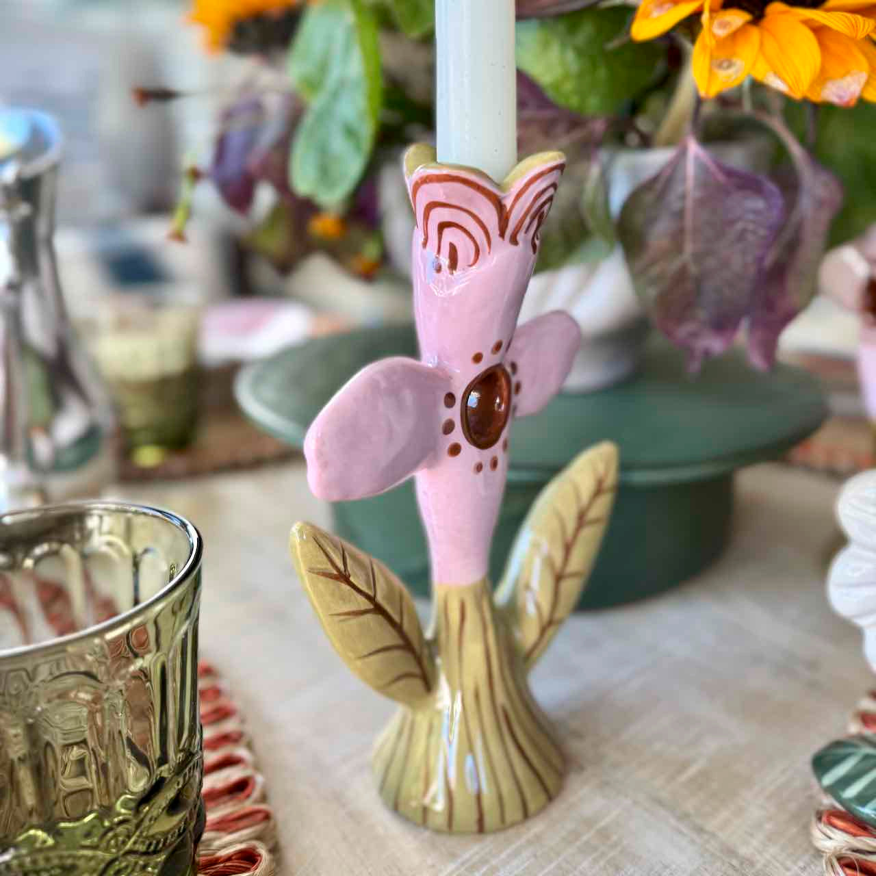 Decorative candle holder shaped like a pink flower with green leaves on a table.