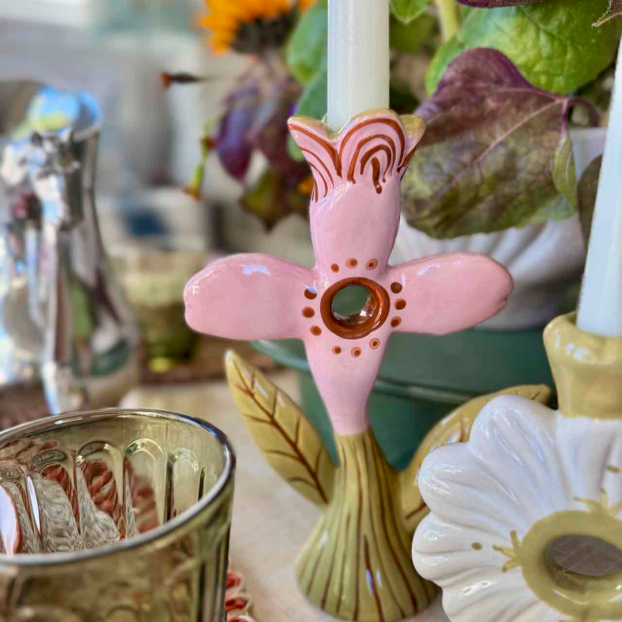 Decorative pink and brown ceramic candle holder with a white candle on a table with other decorative items.