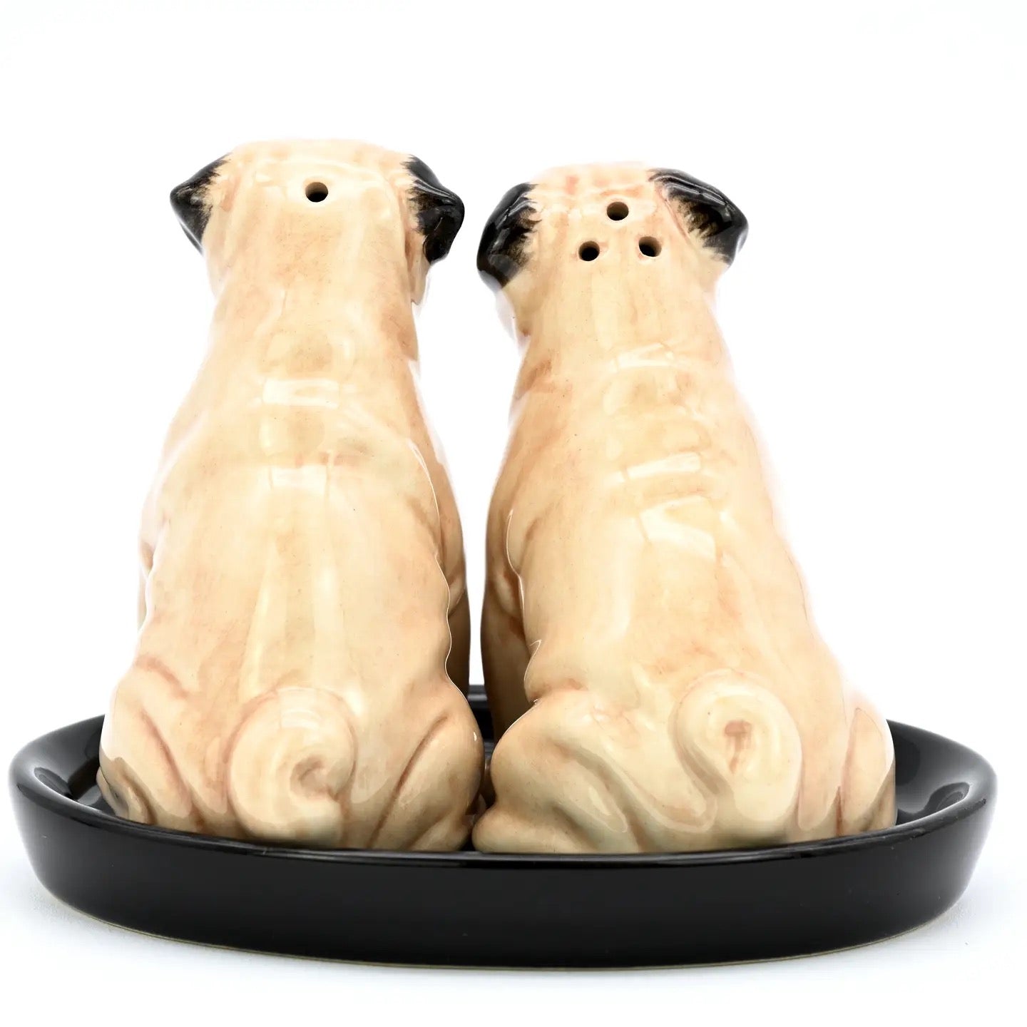 A pair of ceramic pug-shaped salt and pepper shakers sitting side-by-side on a round black dish, photographed against a solid white background.