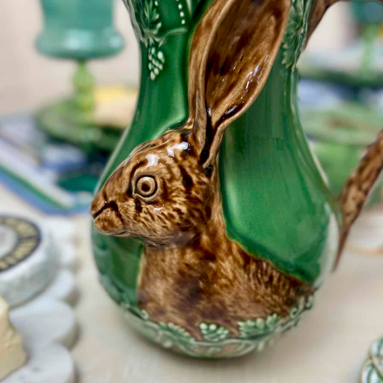 Ceramic rabbit-shaped vase with green body and brown details on a blurred background