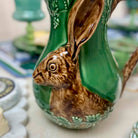 Ceramic rabbit-shaped vase with green body and brown details on a blurred background