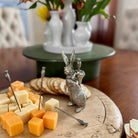 Decorative silver rabbit cheese holder with cheese and bread on a wooden board.