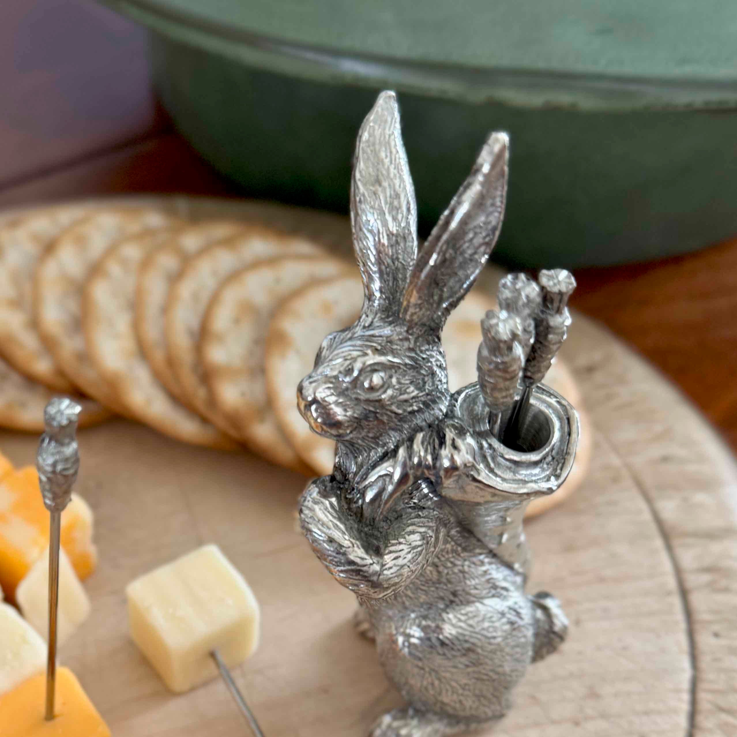 Silver rabbit-shaped cheese pin holder on a plate with cheese and crackers.