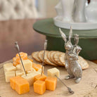 Silver rabbit-shaped cheese knife set with cheese and crackers on a wooden board.