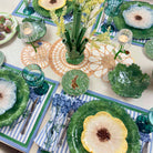 Decorative table setting with green floral plates, glasses, and cutlery on a patterned tablecloth.
