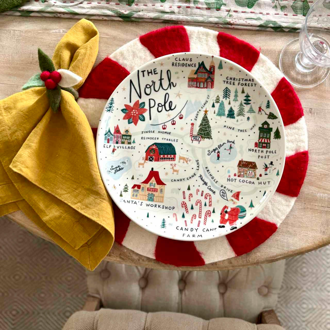 Decorative plate with Christmas-themed design on a table with a yellow napkin.