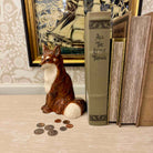 Fox figurine with coins next to books titled 'All The Little Things' and 'Young' on a decorative surface.