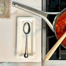 A white rectangular ceramic dish with a printed black spoon and the words 'Serve in Dinner' sits on a light countertop beside a stainless steel pot on a stovetop.