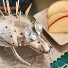 Metallic deer-shaped toothpick holder on a table with sliced apples in the background.