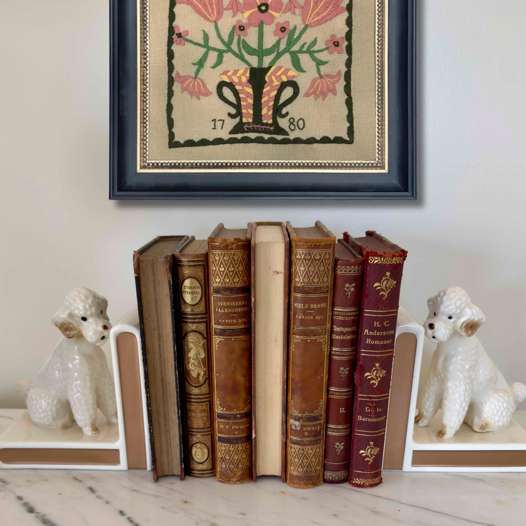 Stack of vintage books with decorative frames and small dog sculptures on a marble surface.