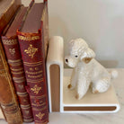 Vintage books with decorative spines and a white ceramic poodle bookend on a shelf.