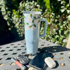 Floral-patterned tumbler on a table with a phone, keys, and lip balm.