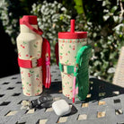 Two patterned water bottles with matching pouches on a table outdoors.