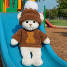 White teddy bear in a brown outfit with a teddy bear design, sitting on a blue slide at a playground.