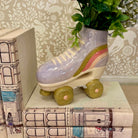 Decorative roller skate with rainbow pattern on a stack of books against a floral wallpaper background