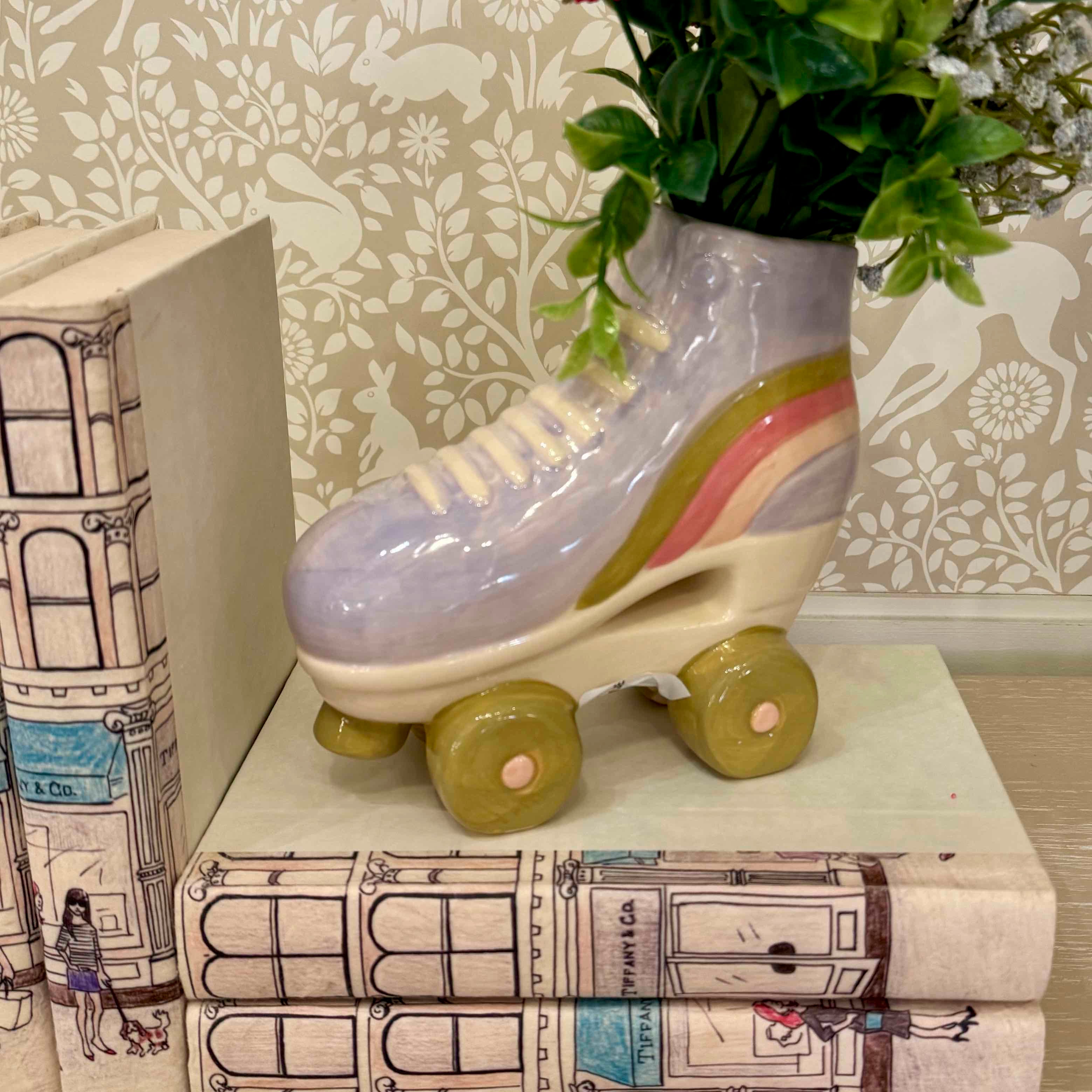 Decorative roller skate with rainbow pattern on a stack of books against a floral wallpaper background