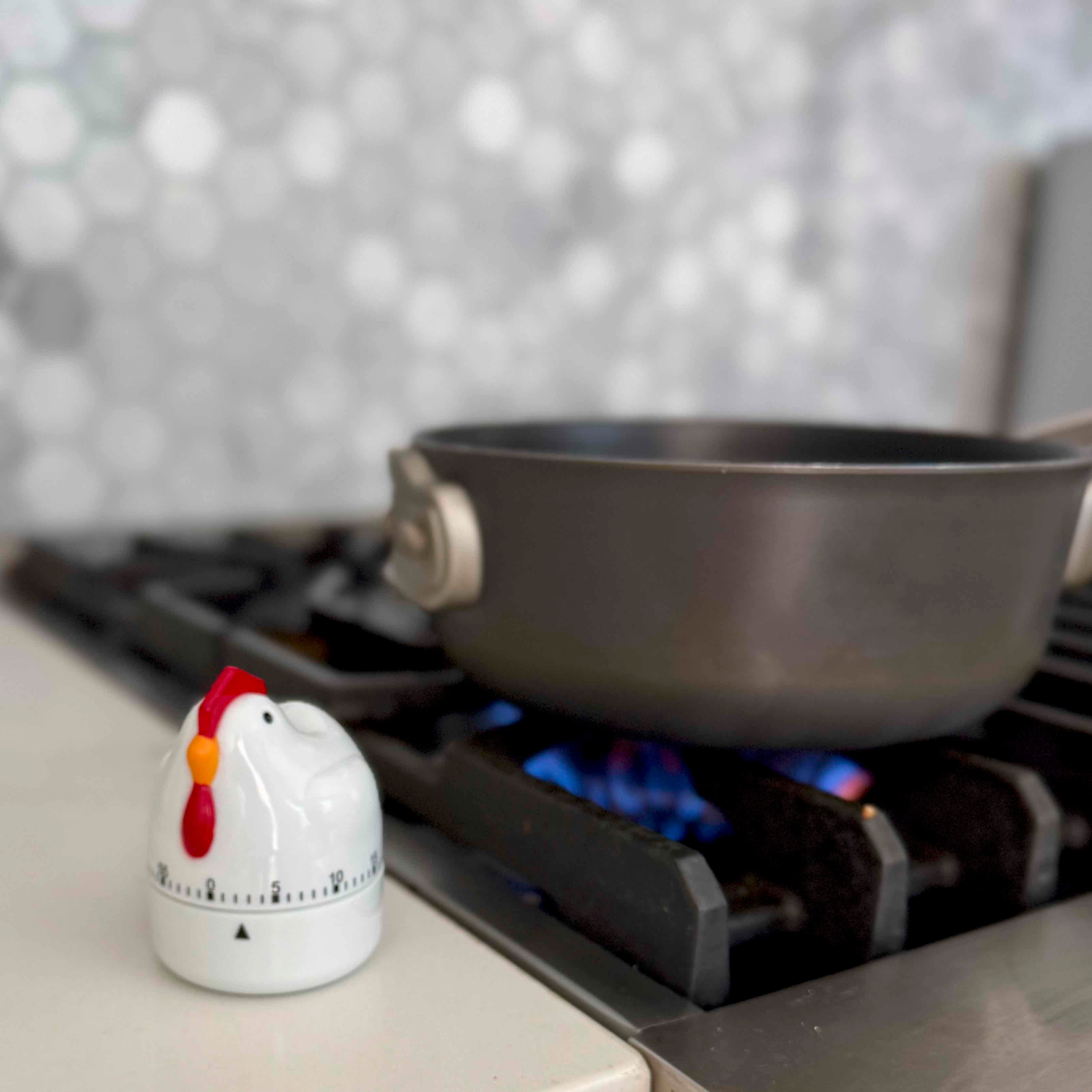Chicken-shaped timer on a stove next to a pot over a flame