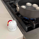 Chicken-shaped timer on a stove next to a frying pan with eggs.