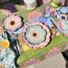 Colorful table setting with floral plates and placemats on a patterned tablecloth.