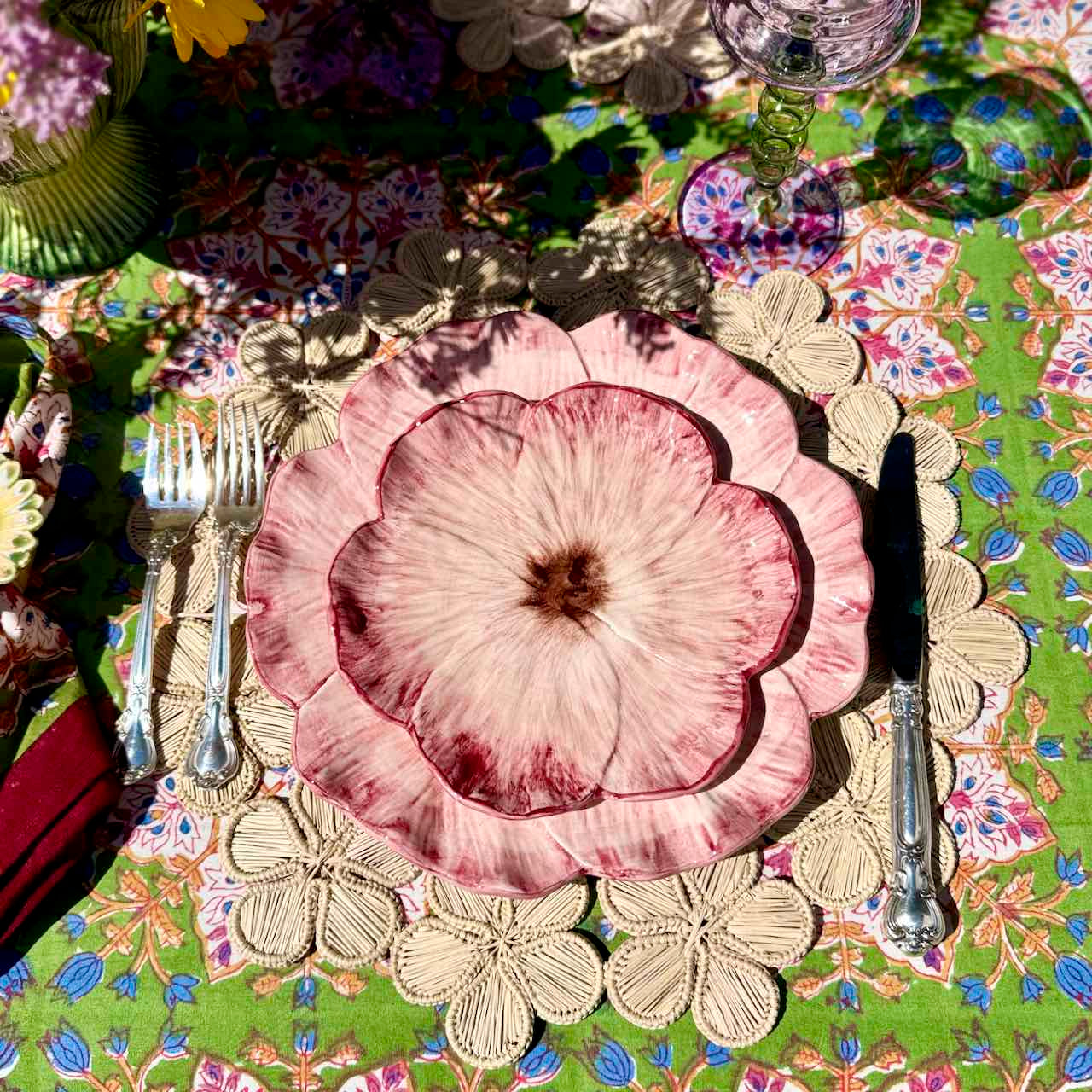 Decorative table setting with floral plates and cutlery on a colorful tablecloth.