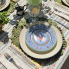 Decorative table setting with floral plates, cutlery, and a patterned tablecloth.