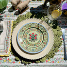 Decorative table setting with a floral plate on a green lace doily, surrounded by cutlery and glasses.