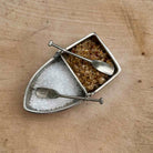 Small metal boat-shaped container with compartments for different types of salt on a wooden surface.