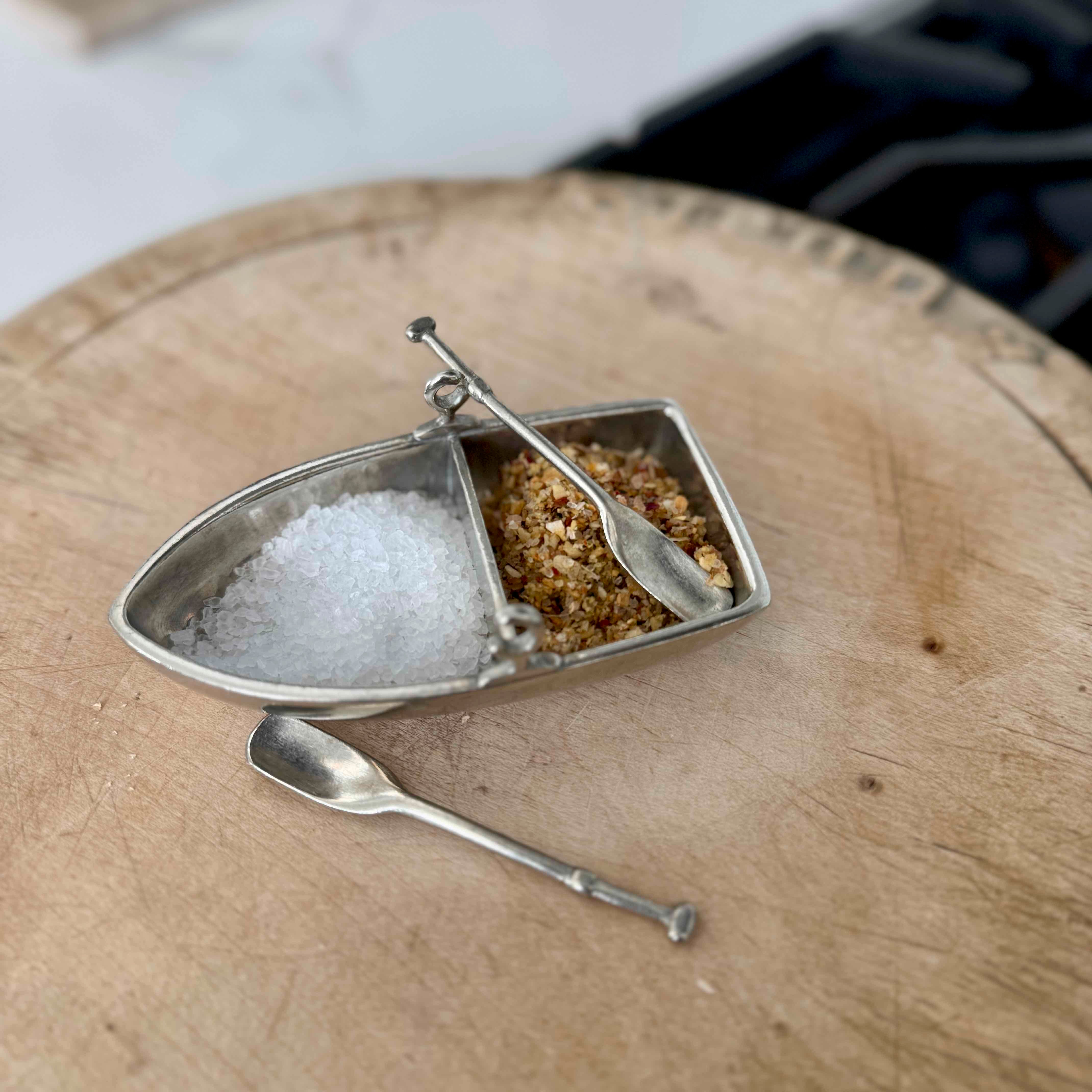 Small metal boat with compartments for salt and pepper on a wooden surface