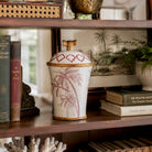 Decorative vase with palm tree design on a wooden shelf with books and plants.