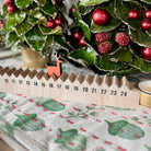 Wooden advent calendar with a small reindeer on a tablecloth with Christmas decorations.