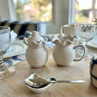 White ceramic pitchers on a table with glasses and plates in the background