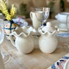 Two white ceramic pitchers on a table with a blurred background