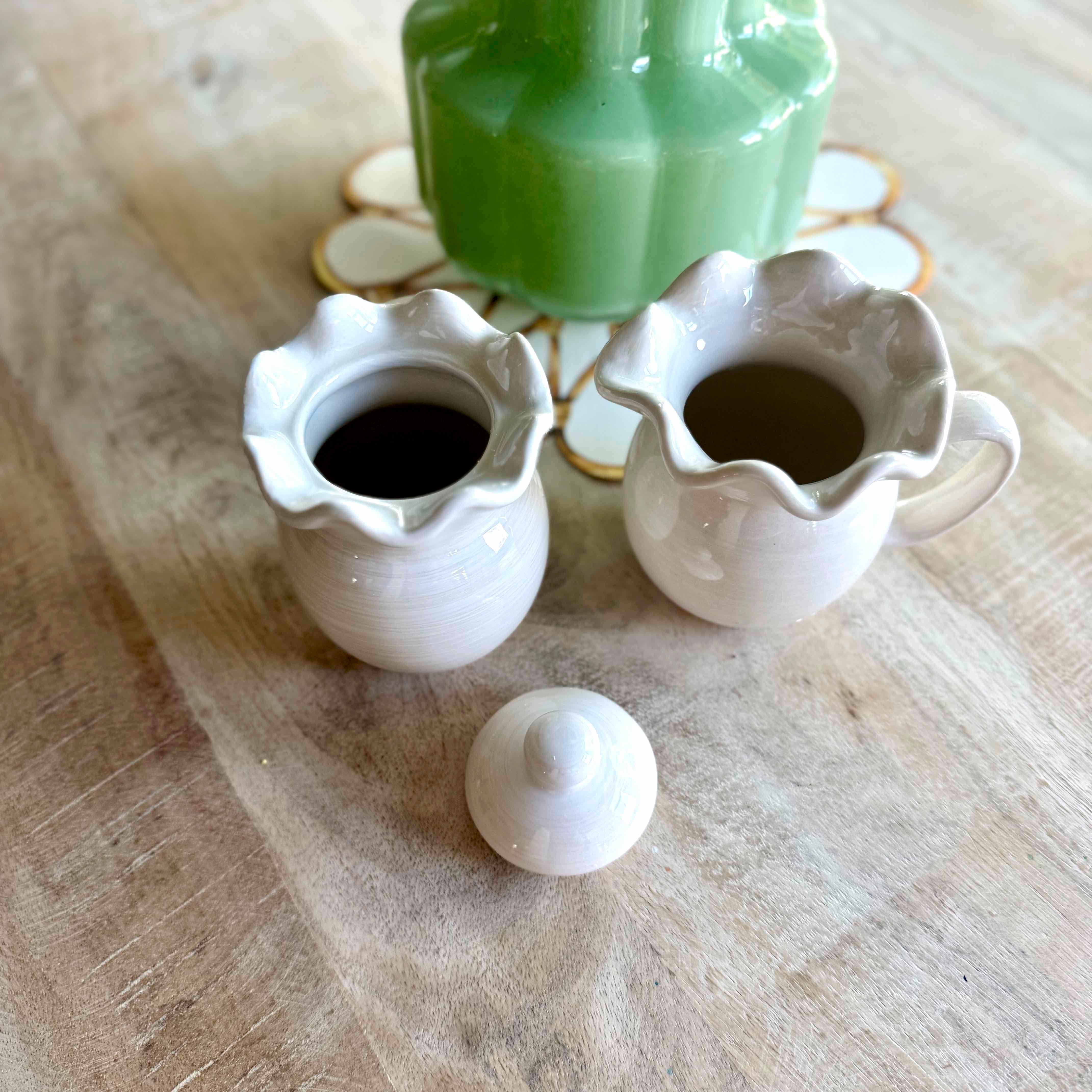 Two white ceramic pitchers with a green bottle on a textured surface