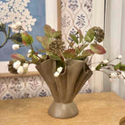 Decorative vase with artificial flowers on a wooden surface with floral wallpaper in the background