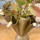 Decorative vase with greenery and white flowers on a wooden surface