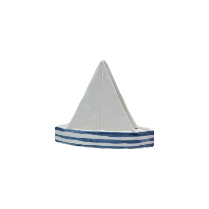 Model sailboat with a white sail and blue stripes on a white background