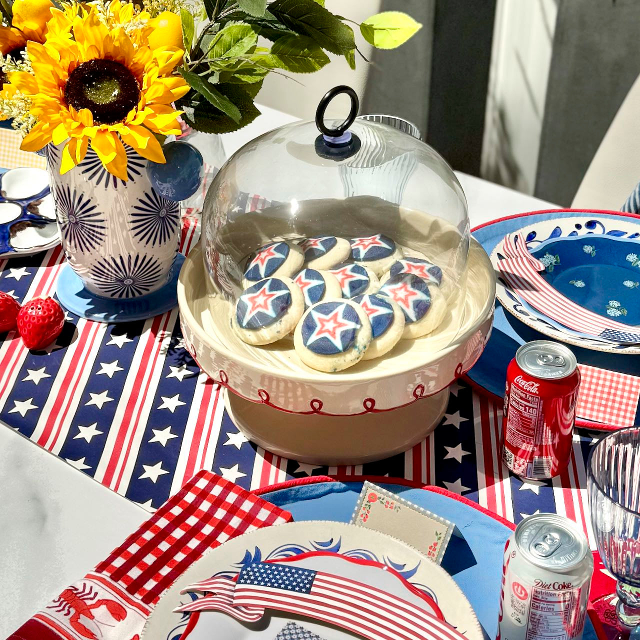 Table setting with patriotic decor, including cookies in a display case and Coca-Cola cans.