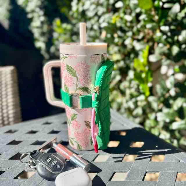 Floral-patterned tumbler with a green sleeve on a table outdoors